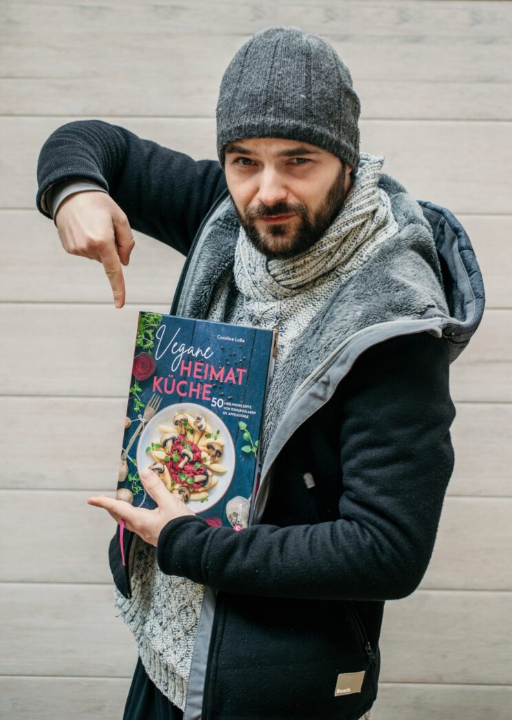 Alexander Büttner zeigt das Kochbuch "Vegane Heimatküche" von Caroline Loße.