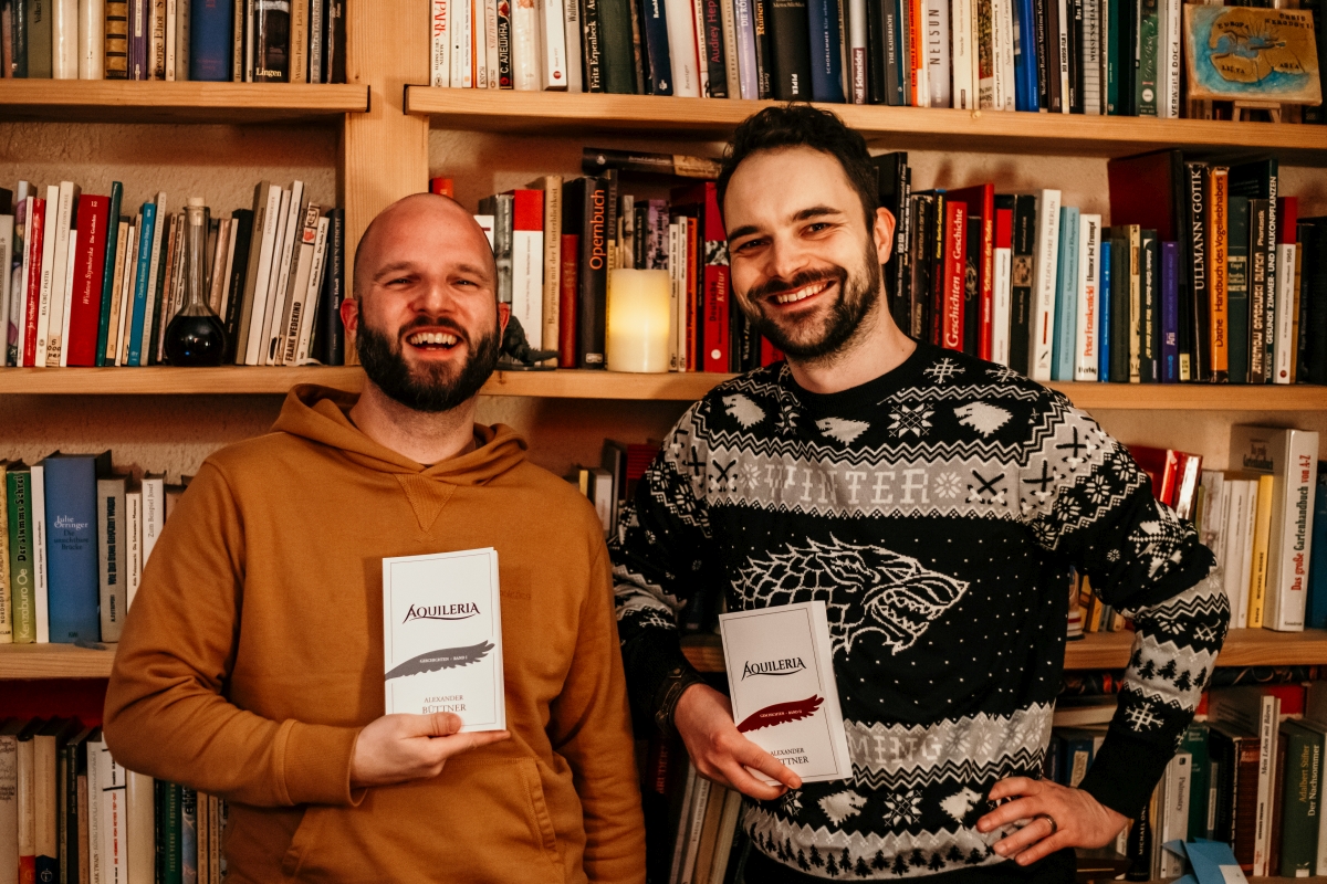 Alexander Senf und Alexander Büttner mit den AQUILERIA Büchern vor einer Bücherwand.