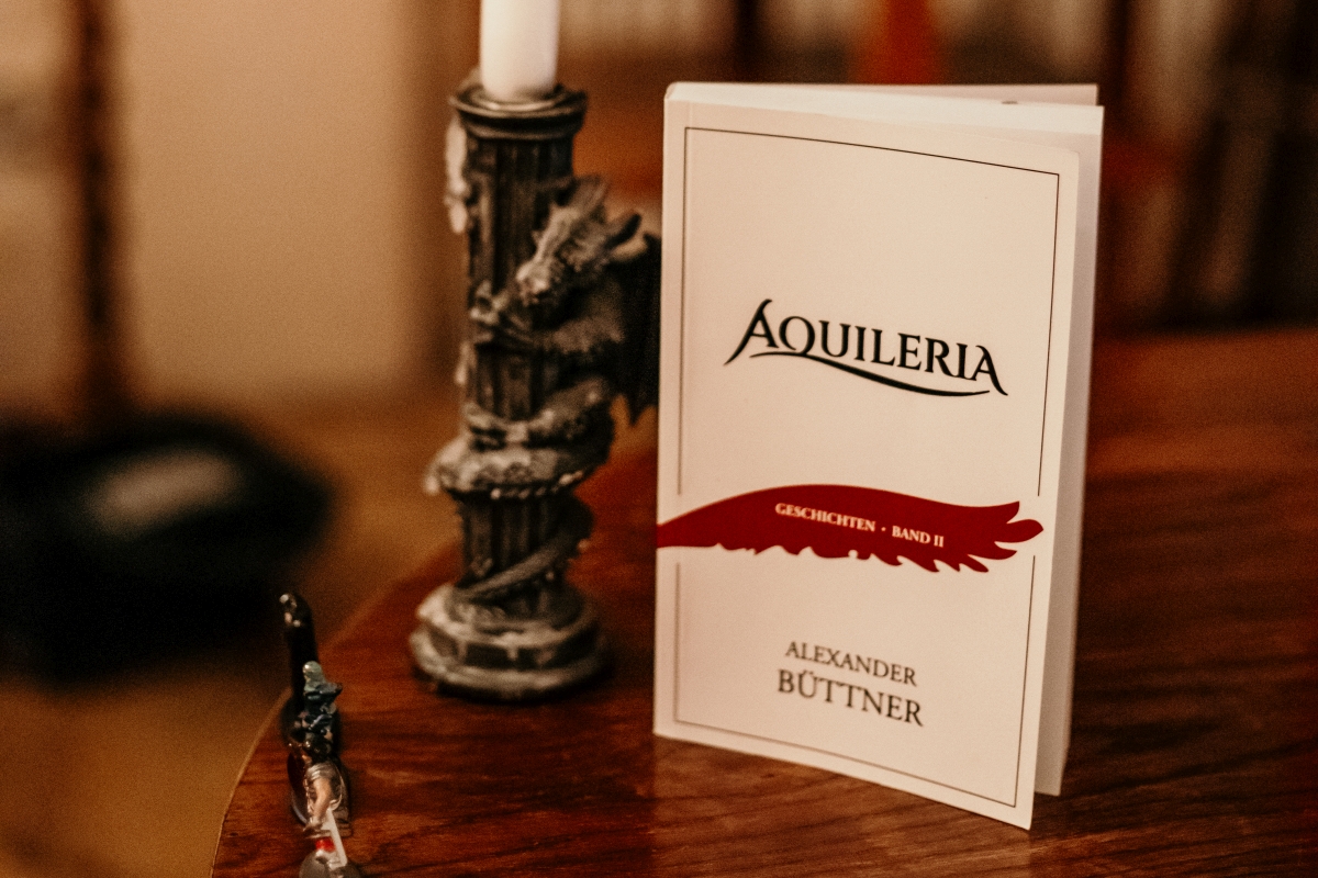 Eine Nahaufnahme von AQUILERIA Geschichten Band II mit einem Drachen-Kerzenständer.